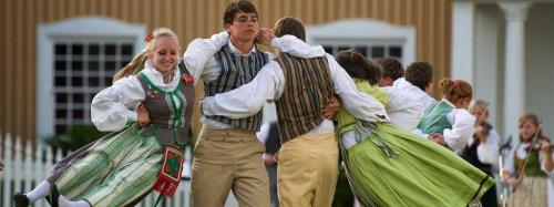 A group of dancers in traditional attire performing a lively dance outdoors, showcasing vibrant costumes and joyful expressions.