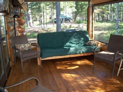 Cozy screened porch with a green couch, two chairs, and a view of a wooded area outside.