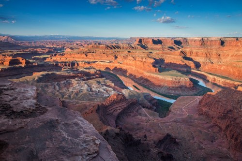 A panoramic view of rugged red rock formations and a winding river under a clear blue sky.