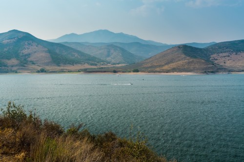 A serene lake surrounded by mountains, with a boat gliding across the water under a hazy sky.