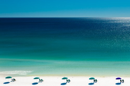 A serene beach scene with colorful umbrellas and chairs on white sand, overlooking a calm turquoise sea.