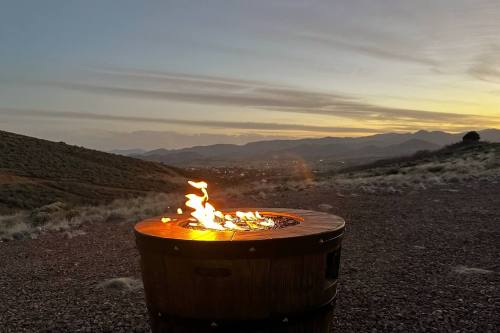 A fire pit with flames, set against a scenic sunset over rolling hills and mountains.