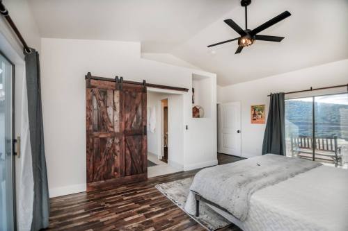 A modern bedroom featuring a wooden sliding door, large windows, and a ceiling fan, with hardwood flooring and neutral decor.