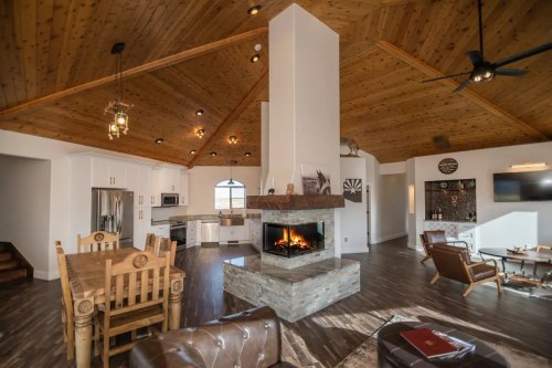 Cozy living space with a stone fireplace, wooden ceiling, and modern kitchen, featuring comfortable seating and warm lighting.