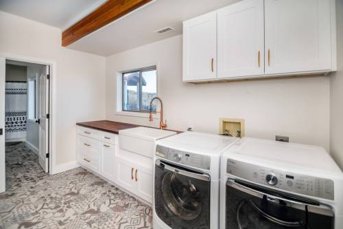 Bright laundry room featuring white cabinets, a farmhouse sink, and modern washer and dryer on patterned tile flooring.