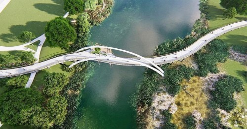 Aerial view of a modern, curved pedestrian bridge over a serene river, surrounded by lush greenery.