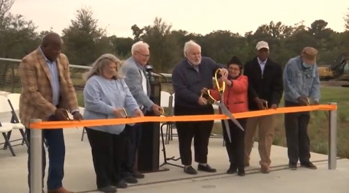 A group of people stands together, preparing to cut a large ribbon at a ceremonial event.