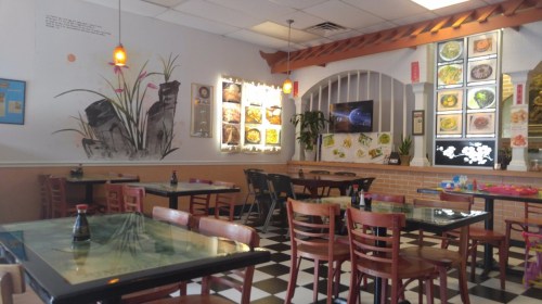 A cozy restaurant interior with checkered floors, wooden tables, and colorful wall decor featuring food images.