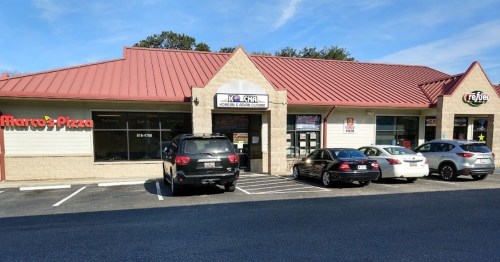 A small shopping plaza with a red roof, featuring a pizza restaurant and a Korean cuisine restaurant, parked cars in front.