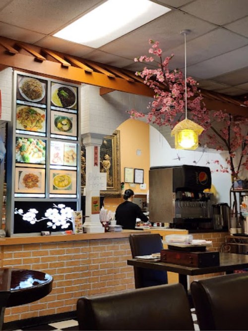 A cozy restaurant interior with a counter, food photos on the wall, and decorative cherry blossom branches.