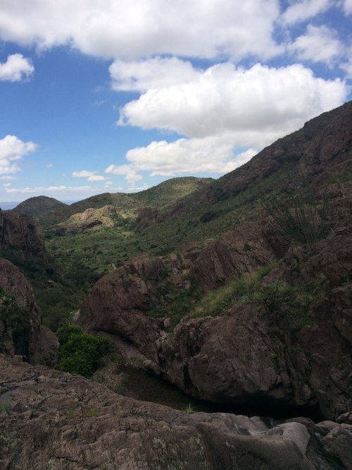 A scenic view of rocky hills and a lush valley under a partly cloudy sky.