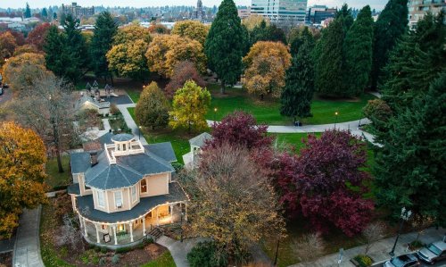 Aerial view of a park with colorful autumn trees and a charming house surrounded by pathways and greenery.