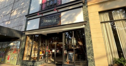 Exterior of a restaurant named "Dumbwaiter," featuring large windows and a welcoming entrance.