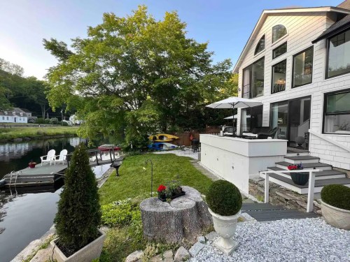 A serene lakeside home with a patio, garden, and dock, surrounded by trees and kayaks.