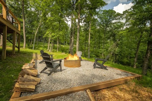A cozy fire pit surrounded by gravel and wooden seating, nestled in a lush green forest.