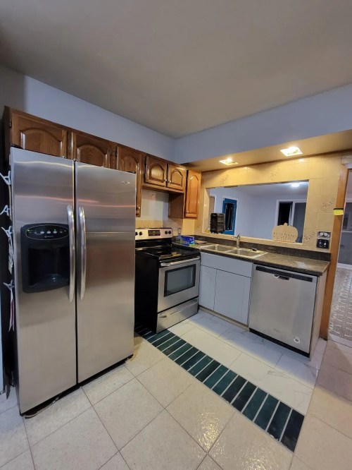 A modern kitchen featuring stainless steel appliances, wooden cabinets, and a tiled floor.
