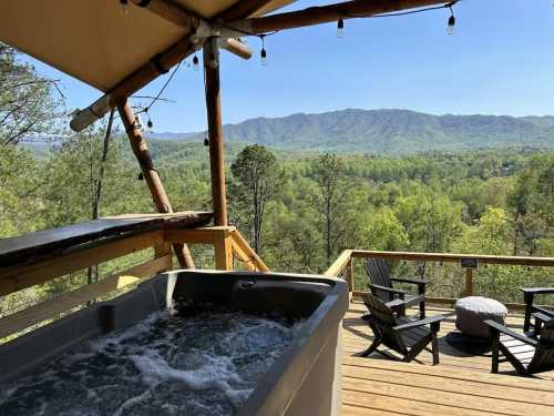 A hot tub on a wooden deck overlooks a lush green landscape and distant mountains under a clear blue sky.