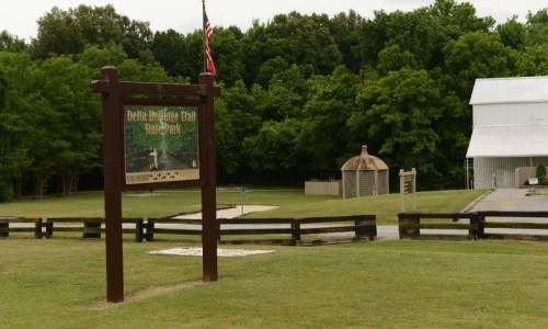 Sign for Delta Heritage Trail State Park with a gazebo and green trees in the background.
