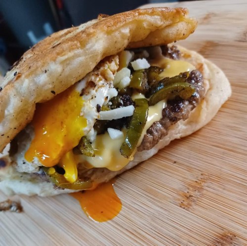 A close-up of a delicious breakfast sandwich with a fried egg, cheese, beef, and green peppers on a toasted bun.