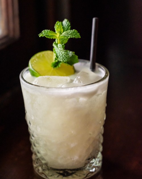 A refreshing cocktail with mint, lime, and ice in a textured glass, garnished with a mint sprig.