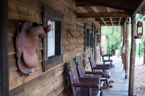 A rustic wooden porch with rocking chairs and a mounted saddle on the wall, surrounded by greenery.