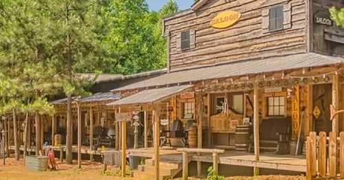 A rustic wooden saloon with a porch, surrounded by trees and a dirt path, evoking a Wild West atmosphere.