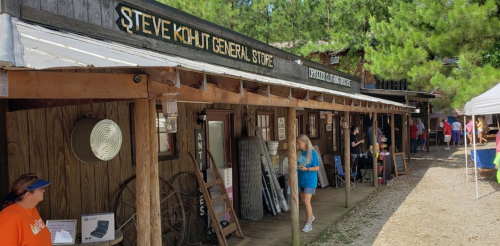 A rustic general store with wooden exterior, people browsing, and a sign reading "Steve Khuht General Store."