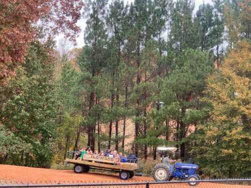 A tractor pulls a wagon filled with people through a wooded area with colorful autumn foliage.