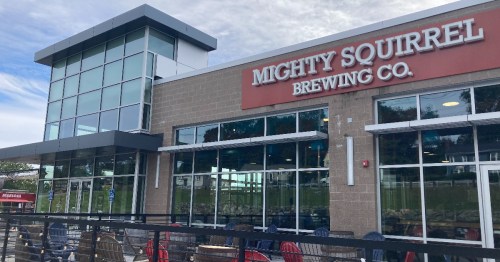 Exterior of Mighty Squirrel Brewing Co. featuring large windows and a modern design. Outdoor seating visible.