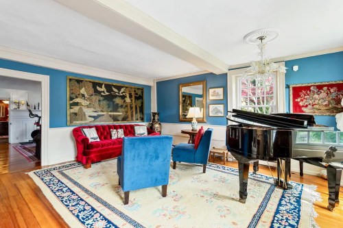 Cozy living room with a red sofa, blue chairs, grand piano, and decorative wall art in a bright, inviting space.