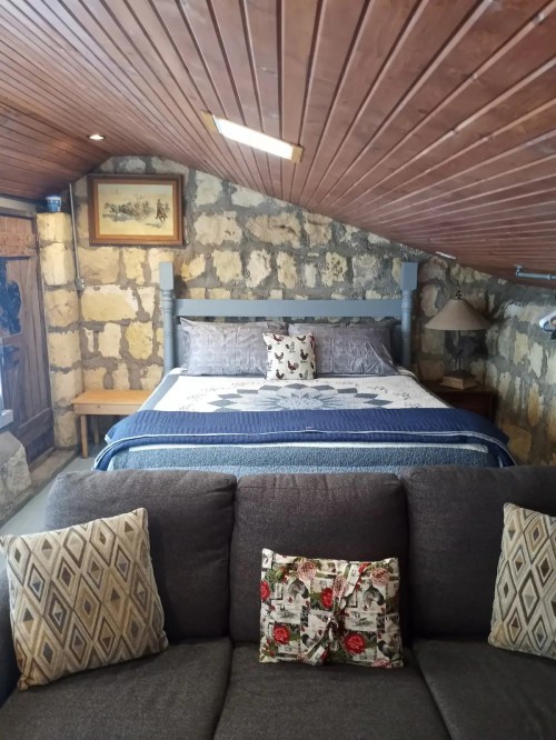 Cozy bedroom with a stone wall, a bed with blue bedding, and a sofa with decorative pillows in the foreground.