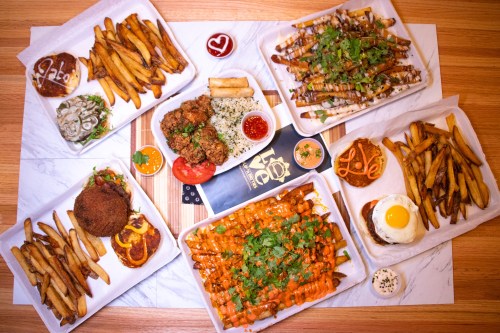 A spread of various dishes including fries, chicken, and loaded fries, arranged on a wooden table with sauces.