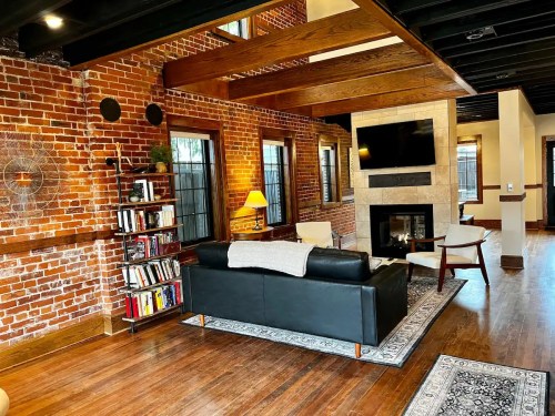 Cozy living room with exposed brick walls, wooden beams, a fireplace, and a black sofa facing a TV.