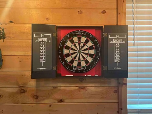 A dartboard mounted on a wooden wall, with scoreboards for the game of cricket on either side.