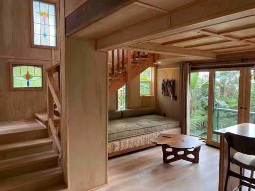 Cozy interior of a wooden cabin featuring stained glass windows, a sofa, and a staircase leading to an upper level.