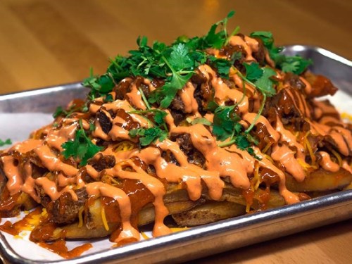 A platter of loaded nachos topped with beef, cheese, cilantro, and a drizzle of spicy sauce.