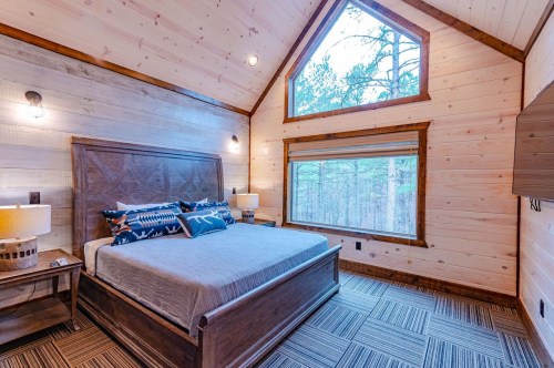 Cozy bedroom with a wooden interior, large window, and a queen bed, surrounded by trees.