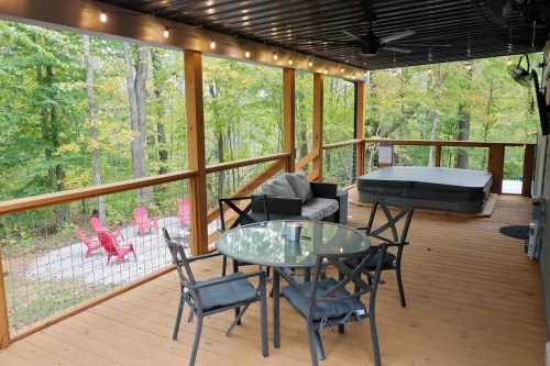 A wooden deck with a hot tub, seating area, and dining table, surrounded by trees and outdoor chairs.