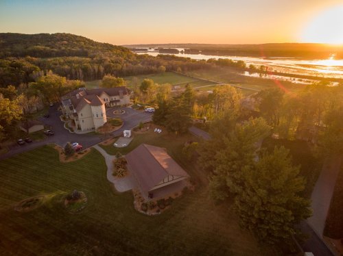 Aerial view of a scenic landscape at sunset, featuring a large building, lush greenery, and a river in the background.