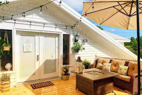 Cozy rooftop patio with a sofa, coffee table, plants, and string lights under a sunny sky.