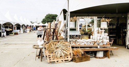 A bustling outdoor market with tents, showcasing decorative items and plants, and shoppers browsing the stalls.
