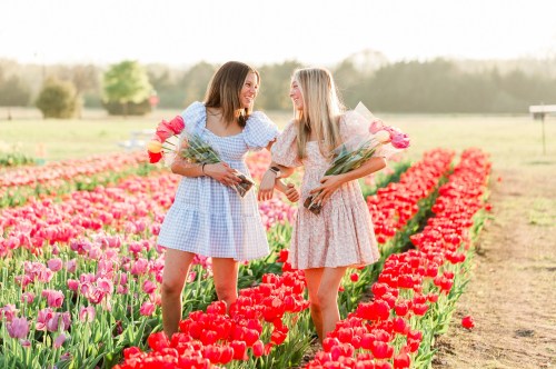 Two young ladies wearing pretty spring dresses, holding bouquets of tulips standing among a field of colorful tulips at a tulip festival in Texas