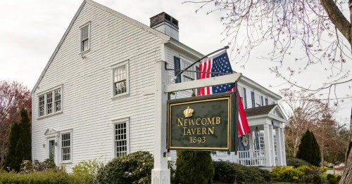 Sign for Newcomb Tavern, established in 1693, with American flags outside a white colonial-style building.