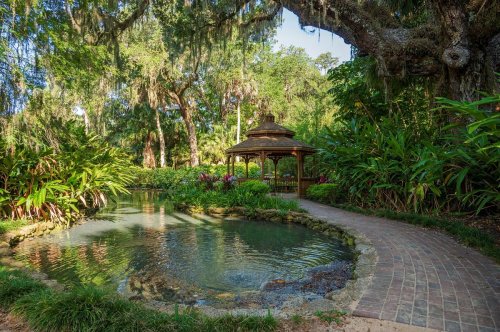 A serene garden scene featuring a gazebo by a pond, surrounded by lush greenery and hanging moss.
