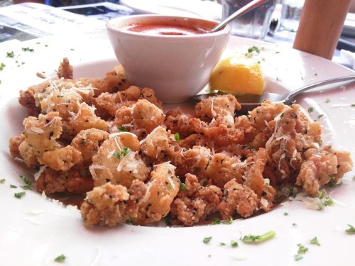 A plate of crispy fried calamari with marinara sauce and a lemon wedge, garnished with parsley and grated cheese.
