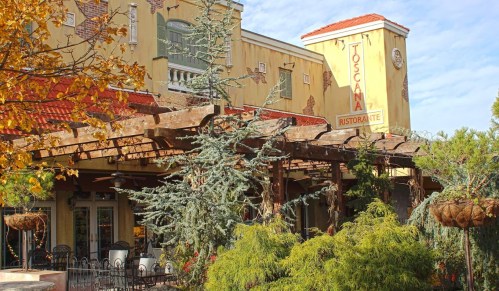 Exterior view of Toscana Ristorante, featuring a rustic pergola, greenery, and a charming yellow building.