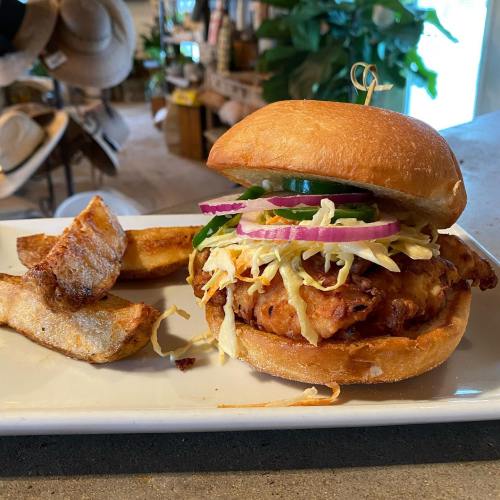 A crispy chicken sandwich topped with slaw and pickles, served with golden fries on a white plate.
