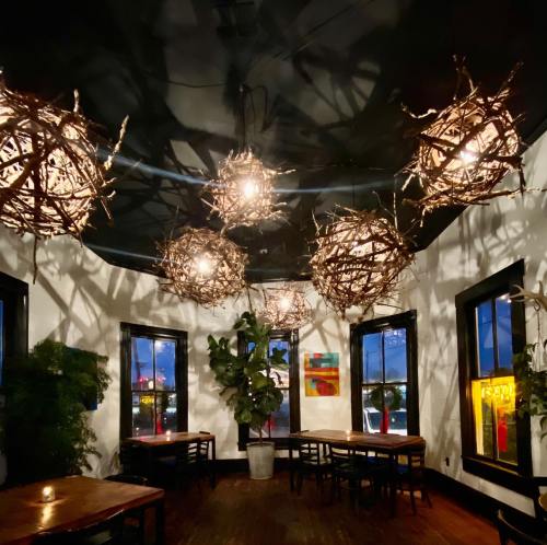 Cozy restaurant interior with unique twig light fixtures, plants, and wooden tables under a dark ceiling.