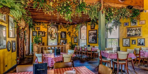 Cozy restaurant interior with yellow walls, checkered tablecloths, and vintage photos, adorned with greenery.