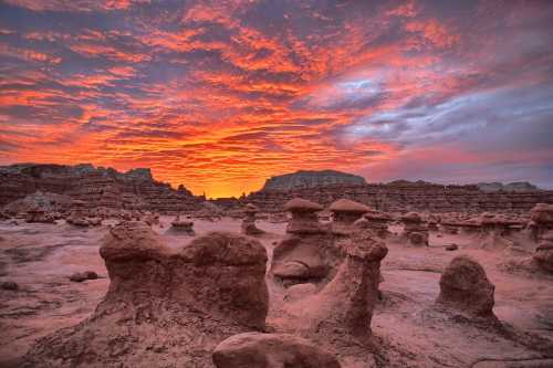 A stunning sunset over unique rock formations in a desert landscape, with vibrant orange and purple clouds.